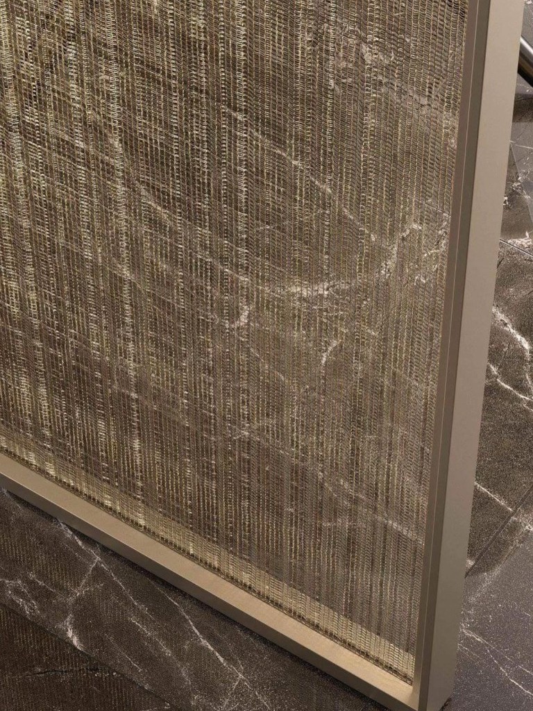 Détail de panneau en maille métallique dorée posé sur sol en marbre veiné, texture verre décoratif à tissu incorporé