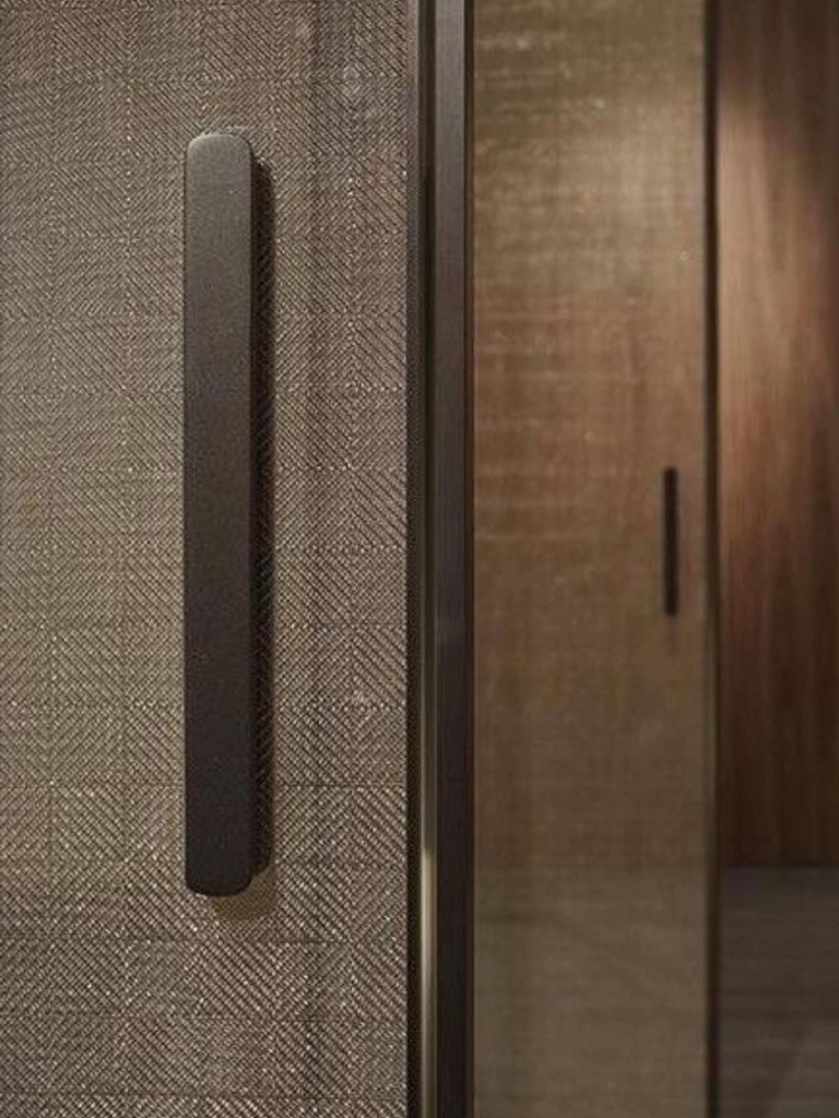 Gros plan poignée verticale bronze sur porte en verre à trame croisée, finition menuiserie premium pour intérieur Maroc